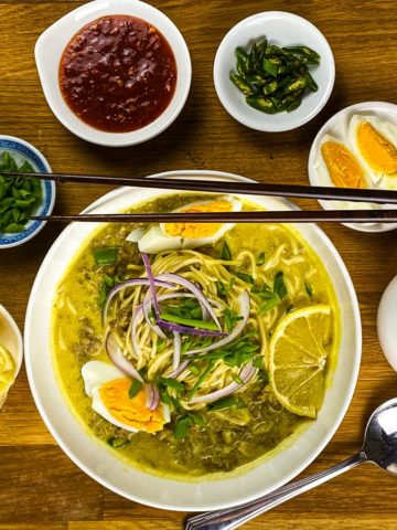 Noodle soup in a bowl with lemon wedges, boiled eggs, cilantro, green chillies, and extra broth