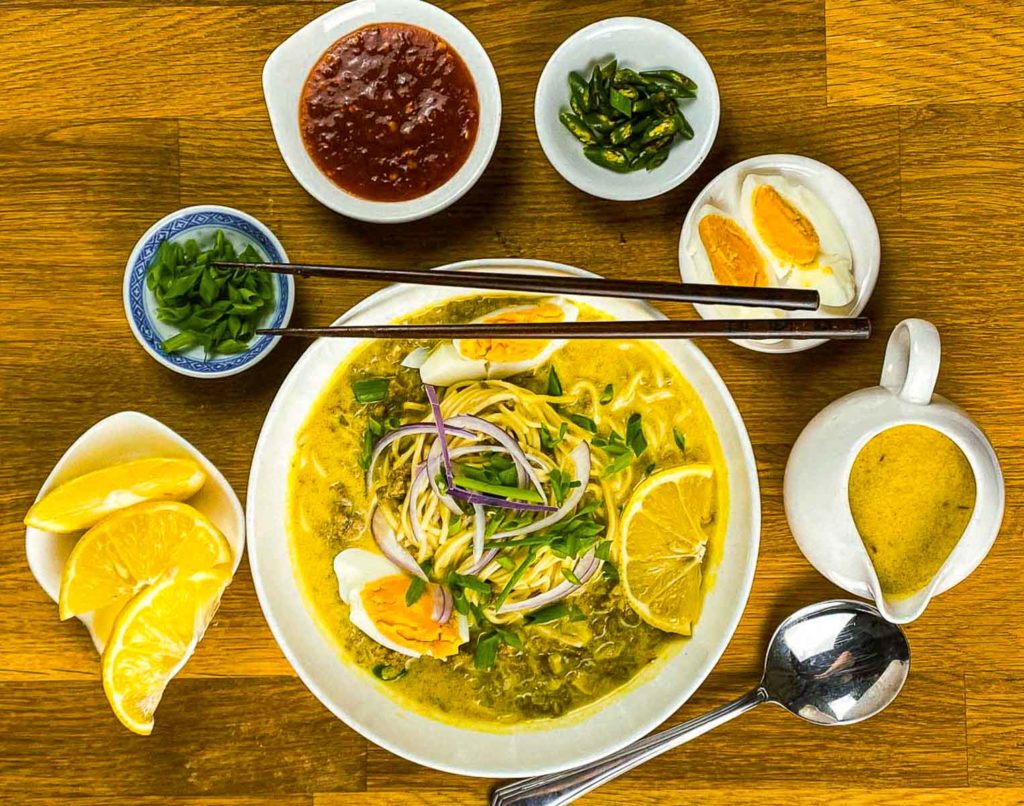 Bowl of noodles with condiments and garnishes on the side.