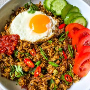 Nasi Goreng Kampung (Indonesian Fried Rice) in a bowl with eggs, tomatoes and cucumbers slices.