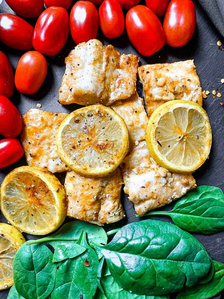 air fryer cod on tray with tomatoes and spinach leaves.