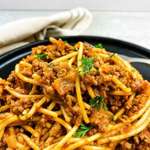 Spaghetti bolognese with garnish on a black plate with a napkin.