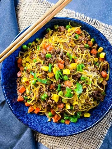 Noodles with vegetables and beef in a bowl with chopsticks.