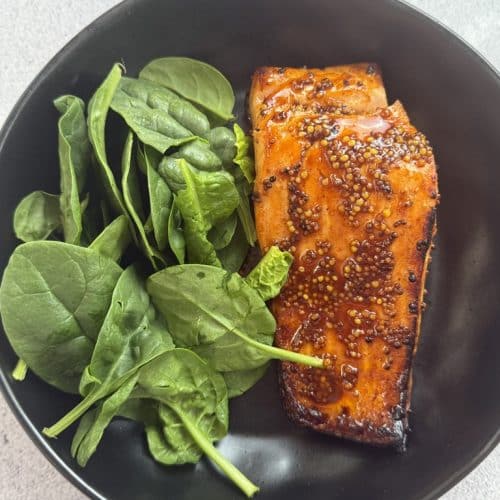 Honey Mustard Salmon In a plate with spinach leaves.
