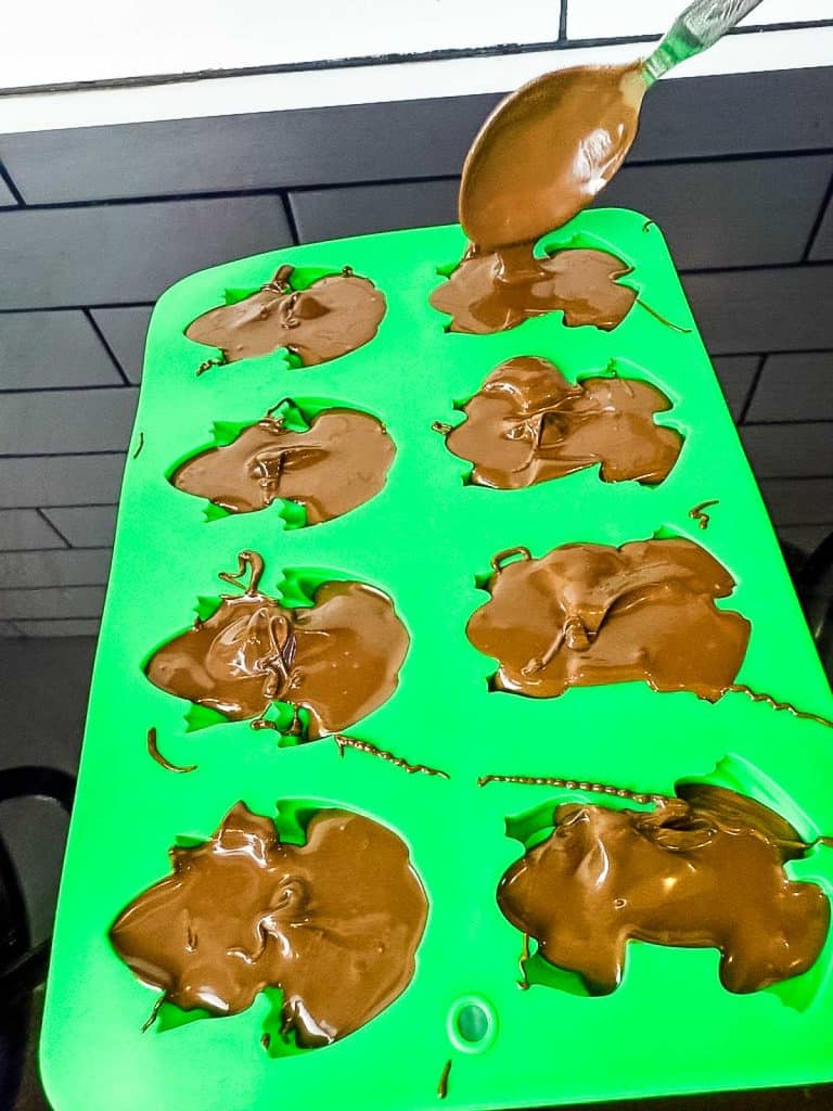 close-up of a spoon pouring chocolate into a frog mold.