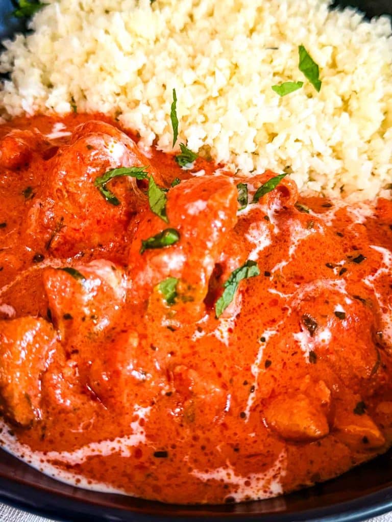 Creamy keto butter chicken in a rich tomato sauce with a butter finish and cilantro garnish with rice