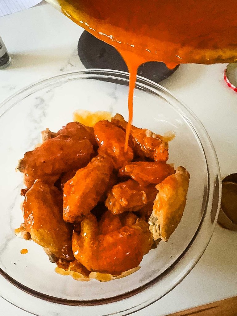 Homemade buffalo sauce being poured over chicken wings